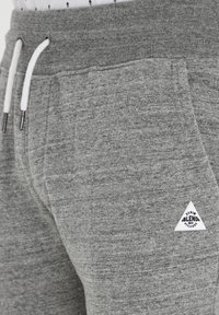Gray sweatpants featuring a ribbed waistband, white drawstring, and a small triangular logo patch on the left side. Smooth texture.