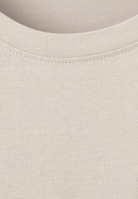 Lyse beige bomuldsstof med en glat tekstur, rund halsudskæring og synlig syning langs kanterne.