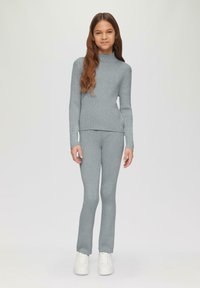 Grijze geribbelde gebreide top met lange mouwen en bijpassende broek, met hoge hals en aansluitend ontwerp, gecombineerd met witte sneakers.
