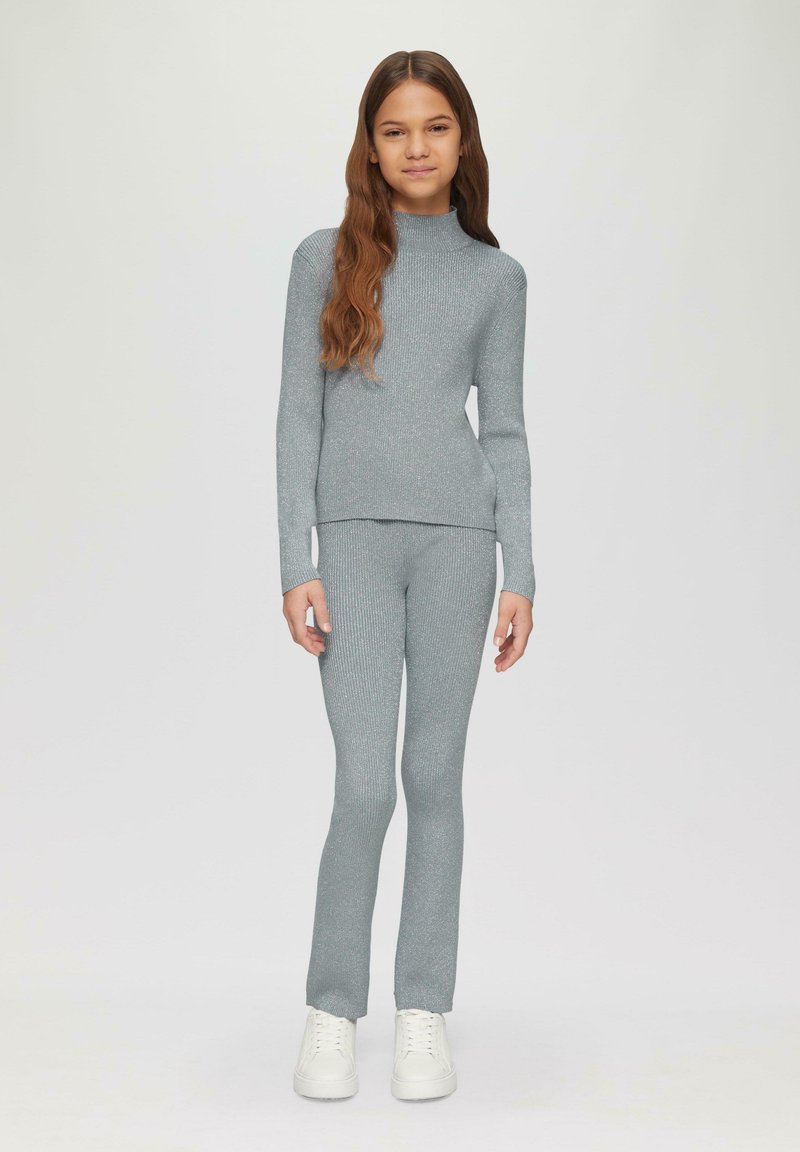 Grijze geribbelde gebreide top met lange mouwen en bijpassende broek, met hoge hals en aansluitend ontwerp, gecombineerd met witte sneakers.