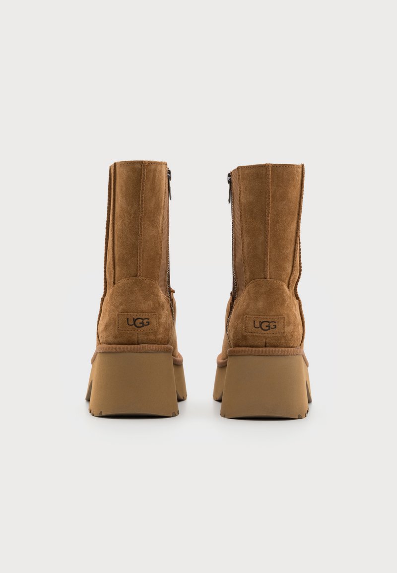 Braune Wildleder-Ankelstiefel mit einem stabilen Absatz, seitlichem Reißverschluss und einem dezenten UGG-Logo auf der Rückseite. Glatte Textur und robustes Design.