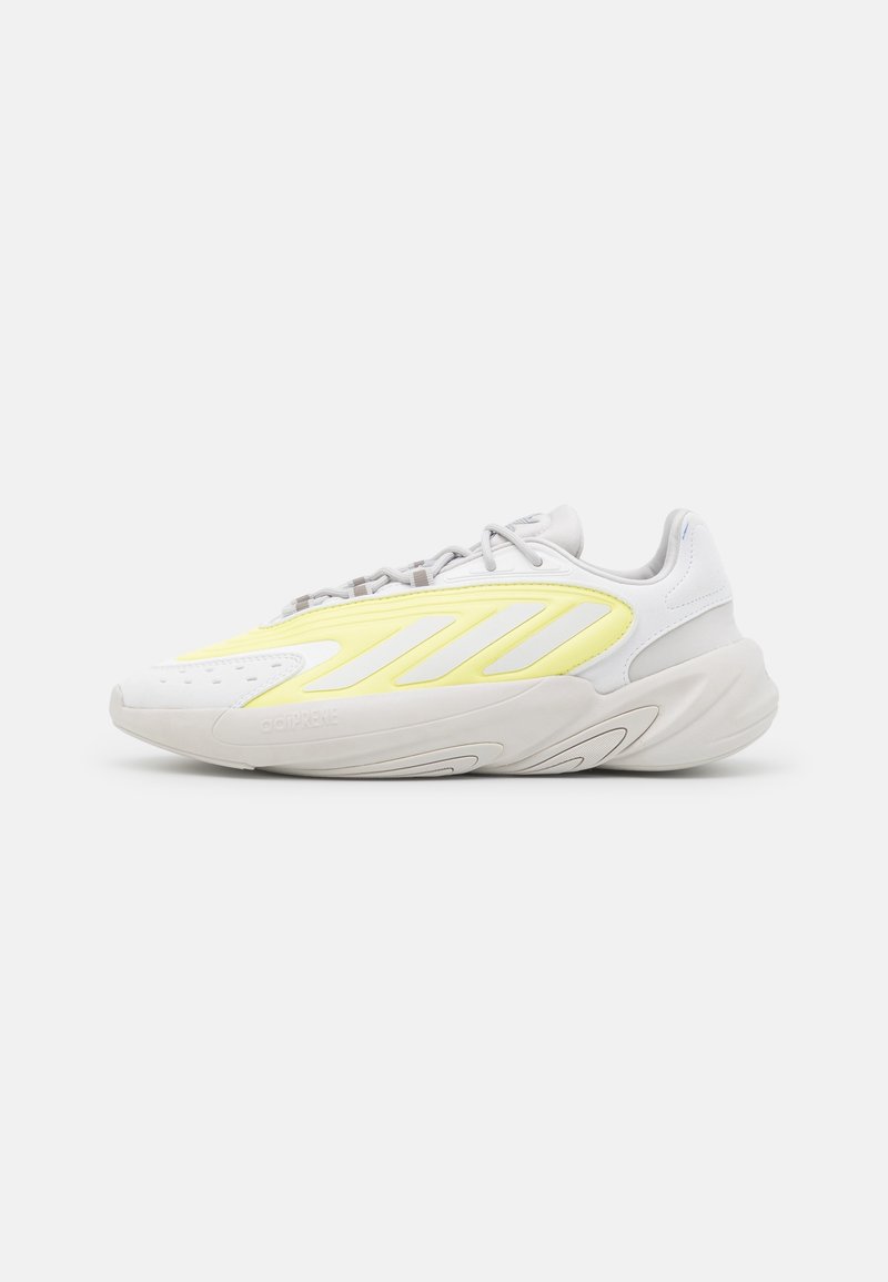 White sneaker with a textured toe, yellow side stripes, and gray laces. Features wave-like sole and "adiPRENE" branding on the side.