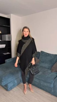 Čierny pončo s textúrovaným zlatým lemom, skombinovaný s čiernymi nohavicami a telovými lodičkami. Na ramene visí malá čierna kabelka.