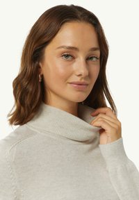 Jasno beżowy sweter z golfem, z prążkowanym dekoltem i mankietami, z delikatnymi detalami tekstury oraz dopasowanym krojem.