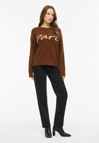 Rudas pūkuotas megztinis su baltu užrašu „Paris“, derinamas su juodais tiesaus kirpimo džinsais ir juodais auliniais batais. Lygus tekstūra ir laisvas siluetas.