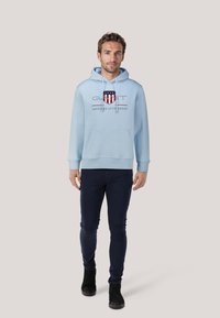 Jasnoniebieska bluza z kapturem z kieszenią z przodu, sznurkami i wzorem logo. Połączona z ciemnoniebieskimi spodniami o slim fit i czarnymi botkami za kostkę.