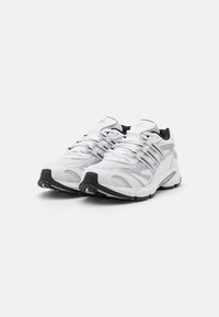 Bāli baltie sporta apavi ar sietiņa augšdaļu, sintētiskajiem ieliktņiem un melno akcentu. Iespējama izcilā mīkstinātā zole un zigzaga saistošā sistēma.