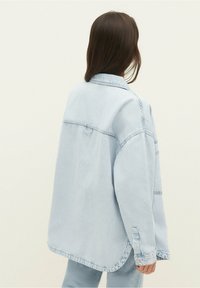 Light blue denim jacket with a relaxed fit, featuring a pointed collar, dropped shoulders, and side slits at the hem. Soft texture.