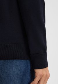 Pull en tricot marine avec des poignets et un ourlet côtelés. Texture lisse avec des détails de couture subtils, associé à un jean en denim.