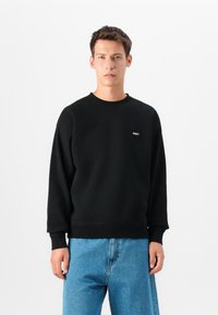 Crna dukserica iz mešavine pamuka, sa okruglim izrezom i rebrastim manžetama, sa malim belim logotipom "OBEY" na grudima.