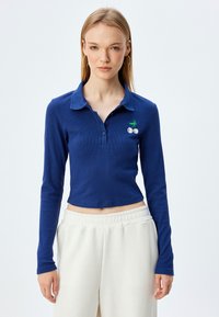 Polo a maniche lunghe di colore navy con texture a coste, dotato di una chiusura con tre bottoni e un design di ciliegia ricamato sul petto.