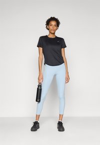 Fekete, rövid ujjú sportpóló és világoskék leggings. A modell fekete vízpalackot tart, fekete sportcipőt visel. Egyszerű dizájn, minta nélkül.