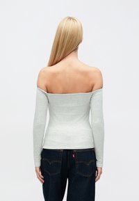 Pelēka, garām piedurknēm, plecu atklājoša augšdaļa no mīksta materiāla, pieguļošs dizains, kombinēta ar tumši zilām džinsa biksēm ar aizmugurējām kabatām.