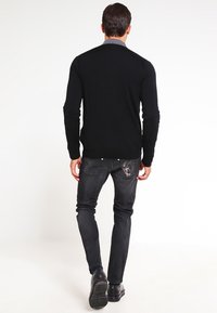 Černý svetr s dlouhým rukávem v kombinaci s tmavými džínami, zdobenými roztrhaným vzorem na zadním kapse, a černými botami. Celkově hladká textura.