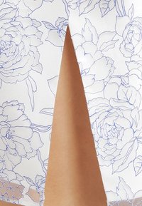 Tessuto a motivi floreali con contorni blu su sfondo bianco, caratterizzato da un dettaglio con spacco che rivela una parte di pelle liscia.