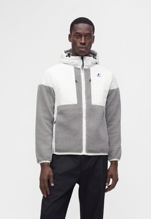 Homme portant une veste polaire blanche et grise avec capuche, debout devant un fond blanc uni, face à l'avant.