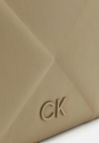 Bežinės odos rankinė su tekstūruotu paviršiumi, su geometriniu raštu ir įspaustu "CK" logotipu apatiniame dešiniajame kampe.