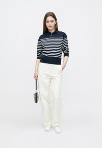 Marineblå og hvitstripet genser med krage, lyse kremfargede bukser, hvite joggesko og en liten svart håndveske. Enkelt design, casual tekstur.