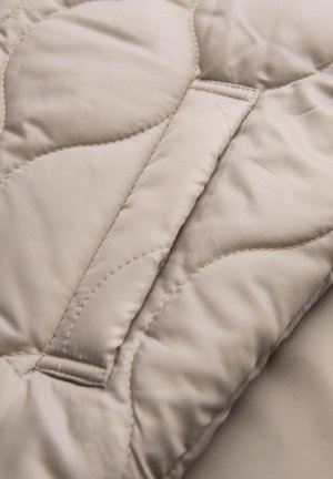 Gequilted beige stof met een gladde textuur en subtiele glans, voorzien van een golvend stikpatroon en een ingevoegd paneel voor structuur.