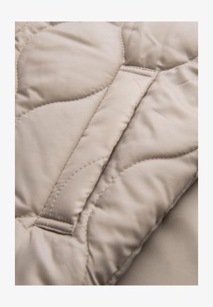 Gequilted beige stof met een gladde textuur en subtiele glans, voorzien van een golvend stikpatroon en een ingevoegd paneel voor structuur.