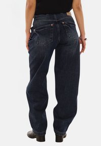 Dark blue denim jeans with a loose fit, featuring two back pockets and copper rivets. The fabric has a slight texture and faded details.