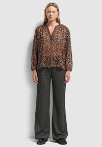 Bruine blouse met luipaardprint, voorzien van een V-hals en lange mouwen, gecombineerd met hooggepantalon grijze wijde broek. Platte zwarte schoenen.