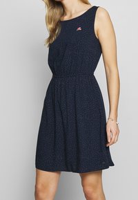 Abito senza maniche blu navy con vita arricciata, piccoli pois multicolori e un dettaglio di ricamo floreale sul petto.