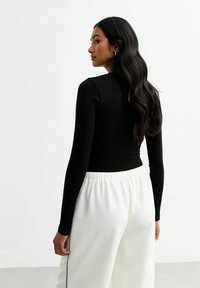 Top negro de manga larga acanalado combinado con pantalones blancos de cordón, exhibiendo un diseño ajustado y un acabado texturizado. Estética limpia y minimalista.