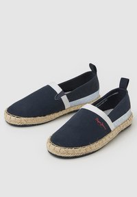 Espadrilles de lona azul marino con detalle de raya blanca, suela de cuerda de yute y acento en rojo del logotipo. Punta redonda y diseño sin cordones.