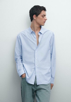Blau-weißer gestreifter Button-Up-Hemd, lange Ärmel, lässige Passform, weicher Stoff, mit kleinem Kragen und einer Brusttasche, kombiniert mit hellen Jeans.