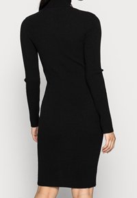 Svart ribbad stickad klänning med hög halsringning, figurnära design, långa ärmar och knälång nederkant. Slät textur och minimal detaljer.