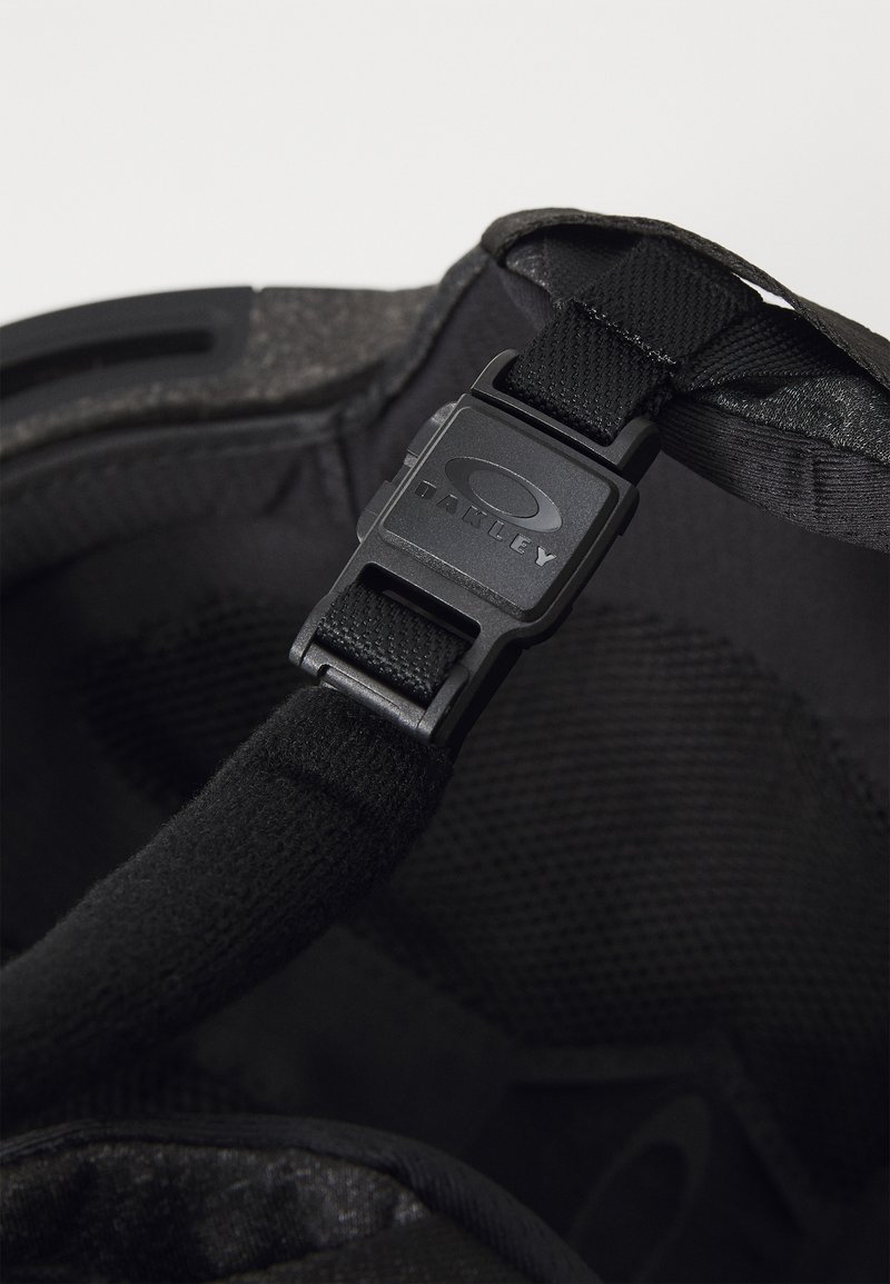 Svart hjälminredning med en stoppad textur, justerbara remmar och en plastspänne med en "Oakley"-logotyp.