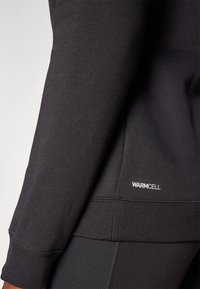 Felpa nera scura con polsini e orlo a coste, con il logo "WARMCELL" in bianco sull'orlo inferiore. Tessuto morbido, design dal taglio casual.