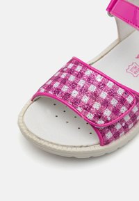 Rosa sandaler med en glittrig rutmönster, med en kardborreband och en solid vit fotbädd. Strukturerad gummisula för bra grepp.