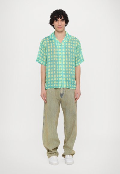 Korte mouwen, groen geblokt overhemd met gele accenten, gecombineerd met losse, lichtgekleurde, gestructureerde jeans en witte sneakers.