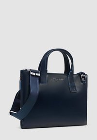 Bolso tote de cuero azul marino con asas dobles, correa de hombro desmontable, acentos en azul contrastante y cierre con cremallera. Detalle del logo visible.