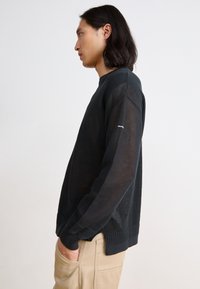 Black mesh sweater featuring a crew neck, ribbed cuffs and hem, and a fitted silhouette. Lightweight and breathable fabric.