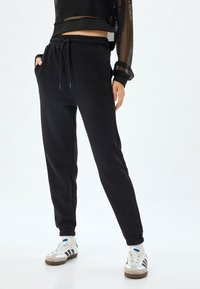 Sorte sweatpants lavet af blødt stof, med en elastisk talje, sidelommer og elastiske manchetter ved anklerne.