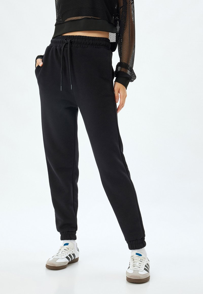 Sorte sweatpants lavet af blødt stof, med en elastisk talje, sidelommer og elastiske manchetter ved anklerne.