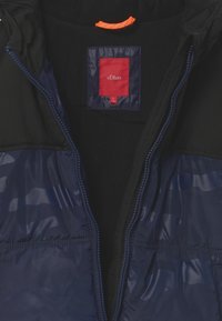 Námořnická modrá a černá zateplená bunda s předním zipem, v přepravním štítku uvnitř límce je červený štítek s nápisem "s.Oliver" a velikostí "S 140".