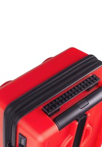 Red hard-shell suitcase with textured black zipper and grip handle. Features a combination lock and smooth, rounded edges.