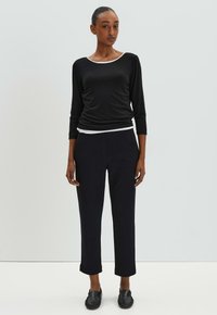 Haut à manches longues noir avec des bordures blanches, associé à un pantalon cropped noir. Les chaussures sont des mocassins noirs. Tissu lisse avec un design ajusté.