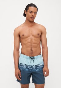 Short de bain en bleu clair et bleu foncé, arborant un imprimé logo audacieux, une taille élastique avec cordon de serrage, et une longueur de short au-dessus du genou.