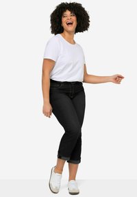 Valkoinen lyhythihainen t-paita yhdistettynä mustiin cropped-farkkusiin, joissa on käännetyt lahkeet ja vaaleat sneakersit, yksinkertaista valkoista taustaa vasten.