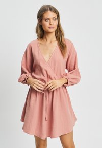 Roza, teksturirana obleka z globokim V-izrezom, dolgimi napihnjenimi rokavi in vrvico za zategovanje v pasu, ki ima sproščen kroj in dolžino do kolen.