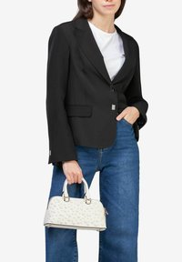 Sort skræddersyet blazer med lange ærmer, to forlommer, parret med en hvid tekstureret handbag med runde detaljer og guldfarvet hardware.