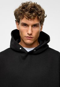 Zwarte hoodie met een trekkoord en zilveren details, gemaakt van een zachte katoenmenging met een relaxte pasvorm en zonder zichtbare patronen.