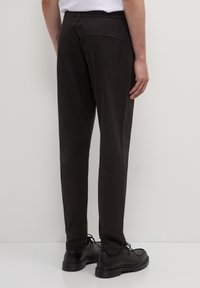 Pantaloni neri con elastico in vita, a taglio dritto, con due tasche posteriori. Indossati con scarpe nere stringate.
