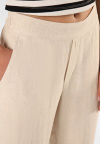Beige Leinenmischungshosen mit strukturierter Oberfläche, seitlichen Taschen und lockerer Passform, gestiktem Bunddetail und weichem Fall.