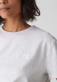 Grijze katoenen T-shirt met een ronde hals, korte mouwen en een subtiele witte logo op de borst. Zacht, textuurstof met een gemêleerd patroon.